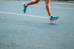 The legs of a runner in blue running shoes as they stride down a paved road. This photo is used on www,becomingstoic.net in an article called "Marathon or Sprint".