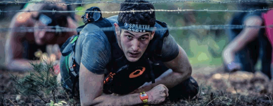 Man crawling through dirt under barbwire in Spartan Race. This photo is used on www.becomingstoic.net in an article named "Building Mental Toughness".